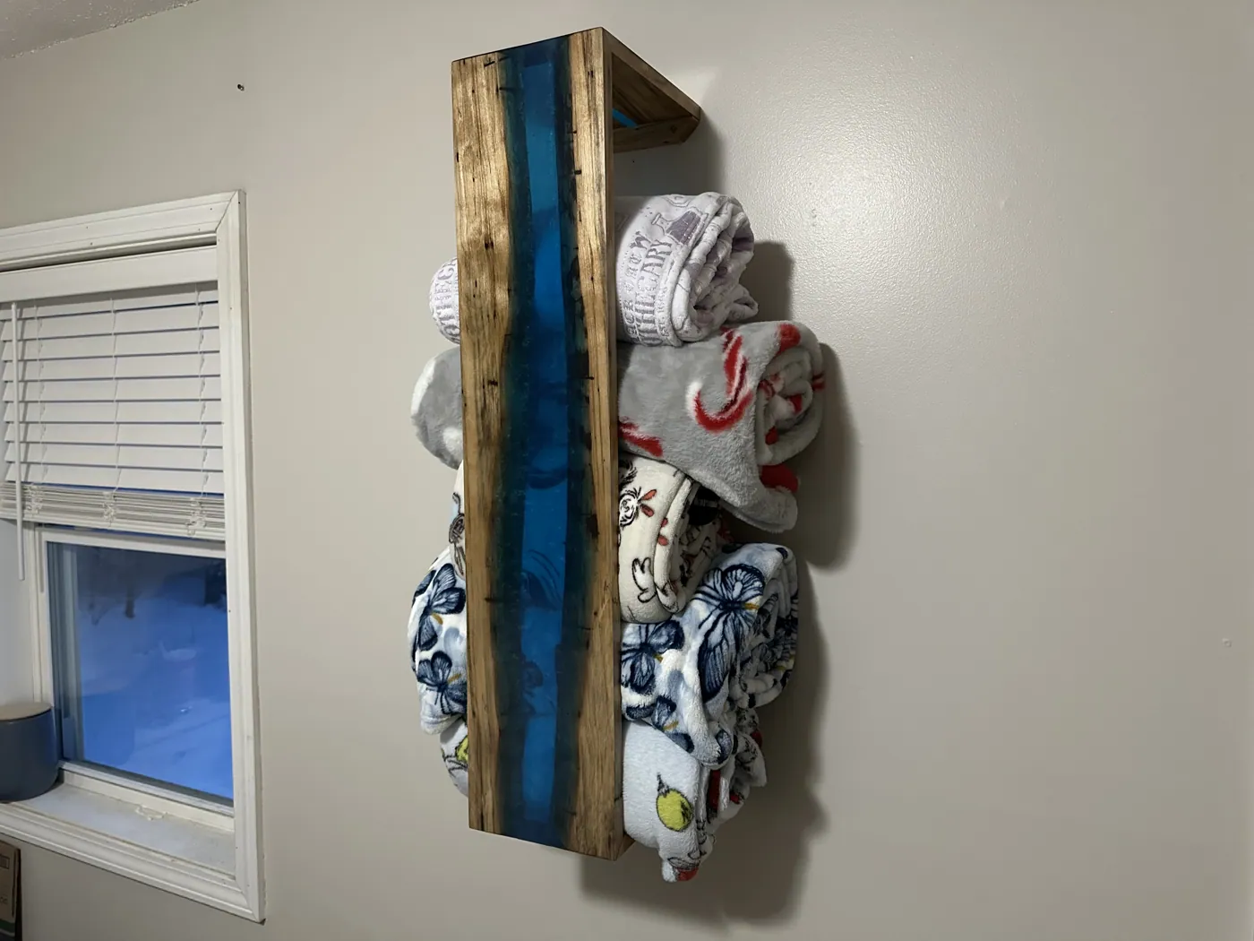 Wall-mounted blanket rack built around a live-edge board with a deep blue resin river.