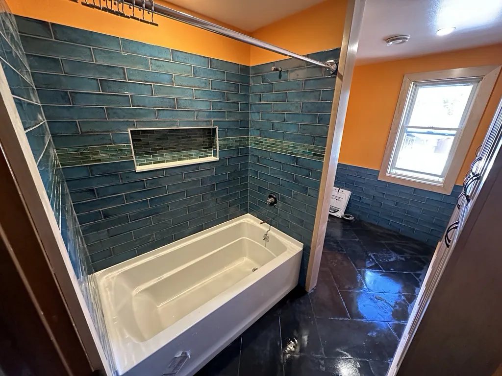 A bathroom remodel finished in teal subway tile with a glass-mosaic niche and slate floor.