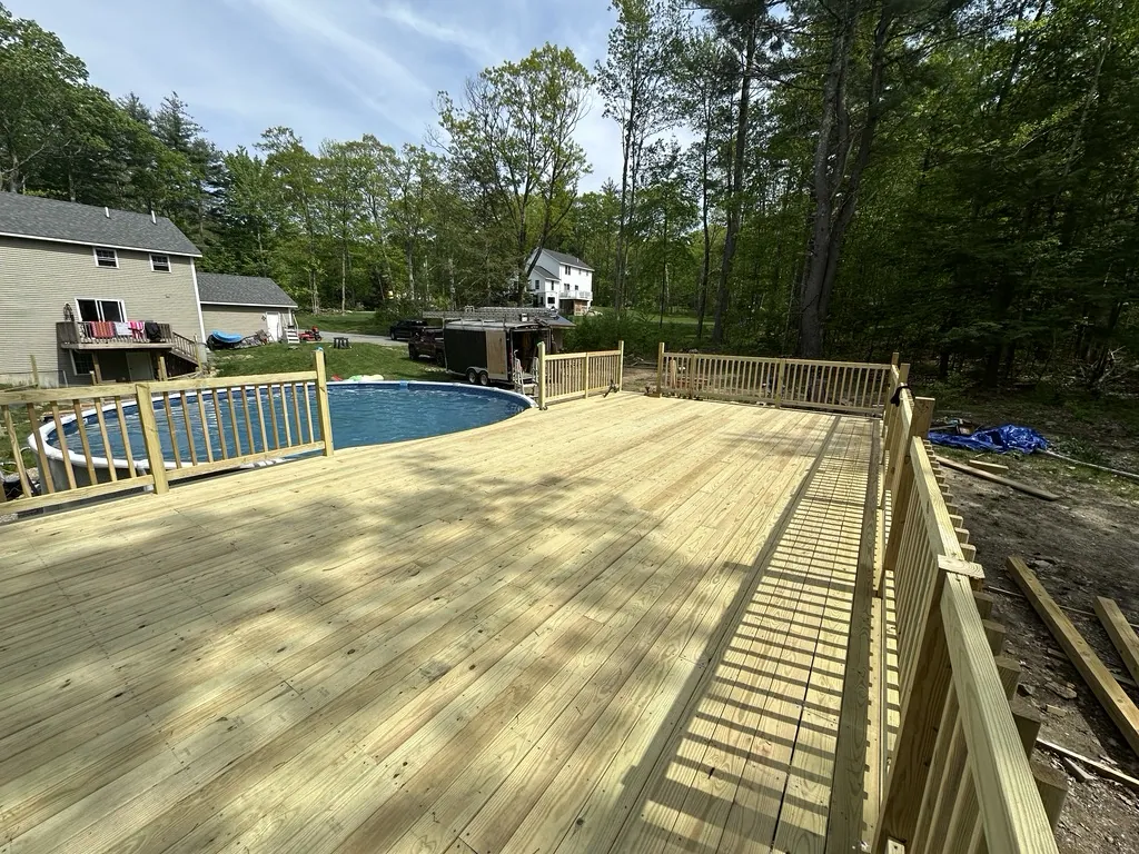 A new pressure-treated deck wrapping an above-ground pool, with full railings.