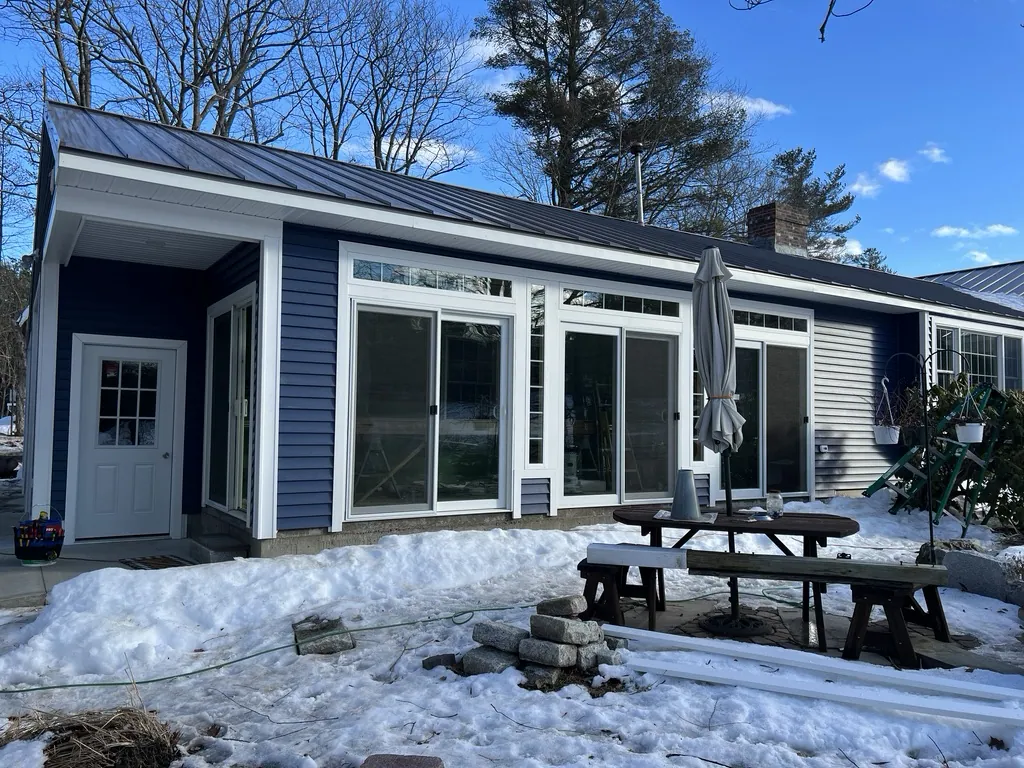 A home addition finished with blue siding, a standing-seam metal roof, and a wide window wall.